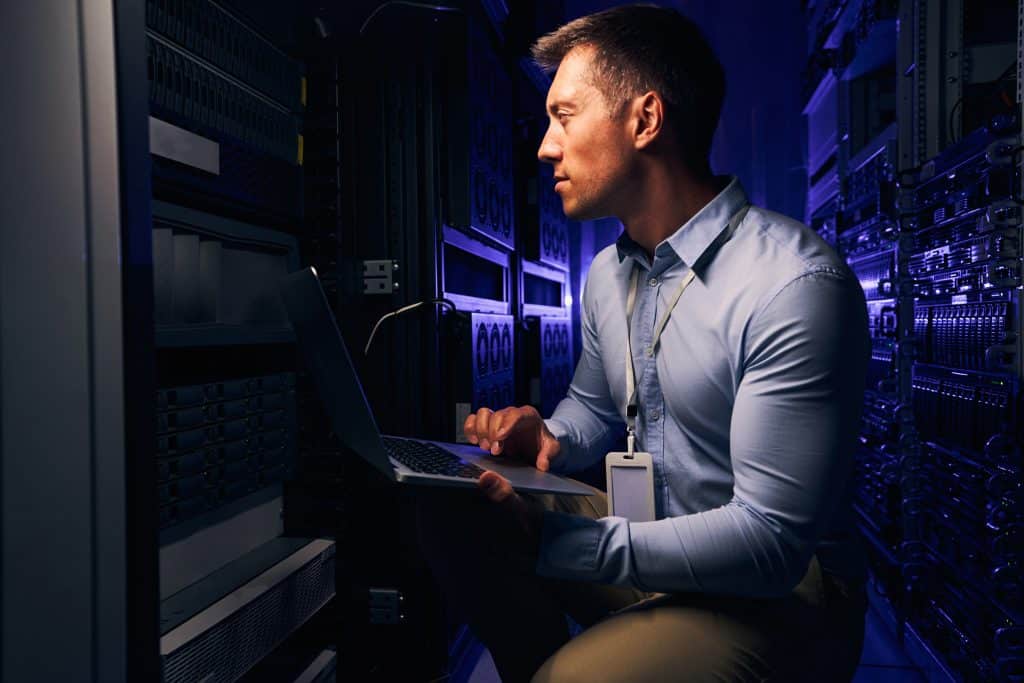 Homem com laptop em mãos verificando um data center