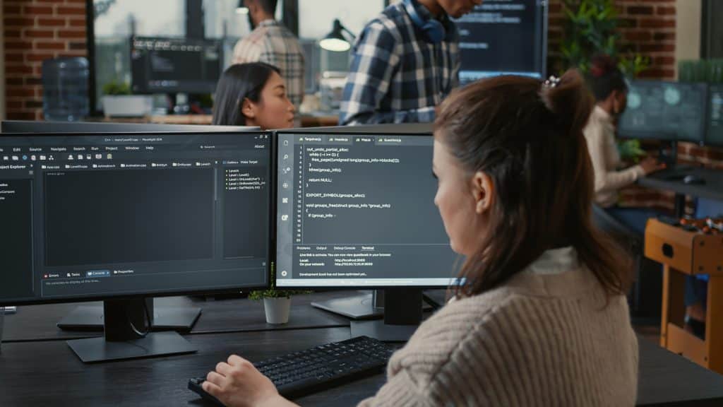 Mulher branca de frente para duas telas de computador programando