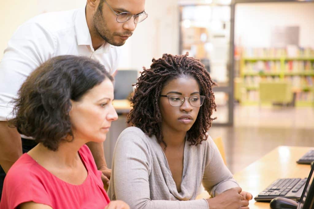 Estudantes em universidades, com livros ao fundo, olhando tela de computador.